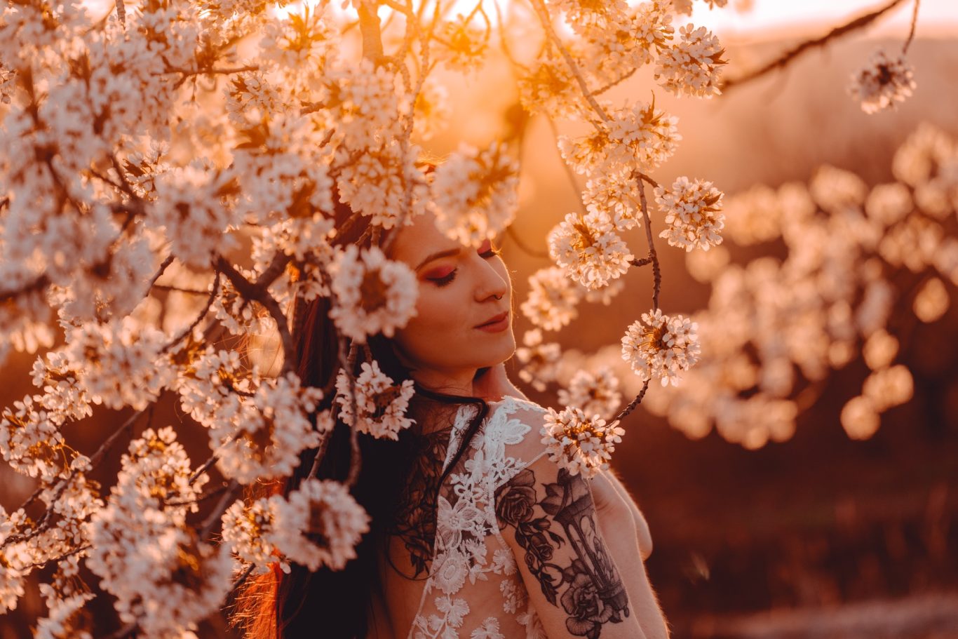 Junge Frau steht vor blühenden Kirschbäumen im warmen Sonnenlicht.