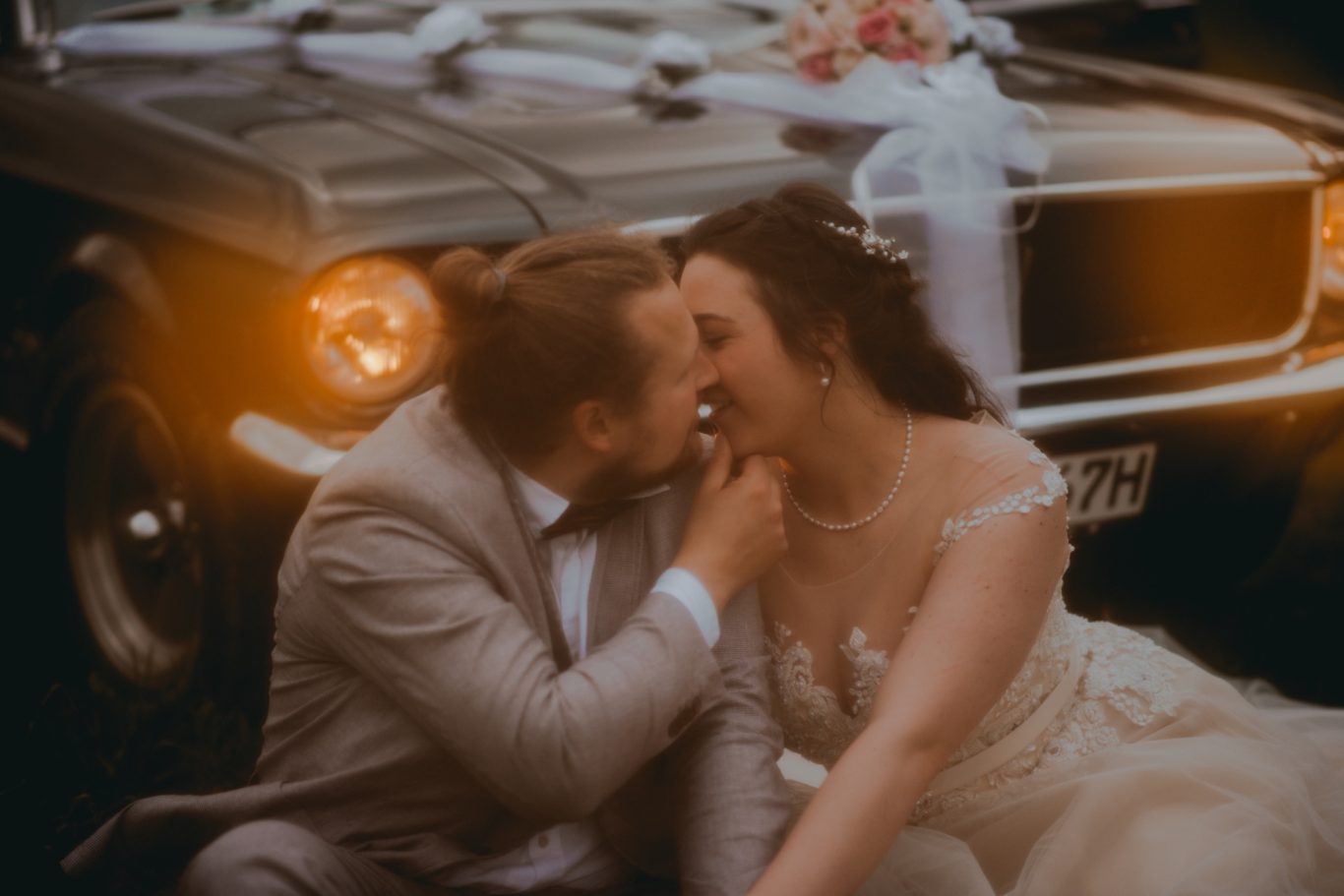 Braut und Bräutigam küssen sich vor einem dekorierten Oldtimer.